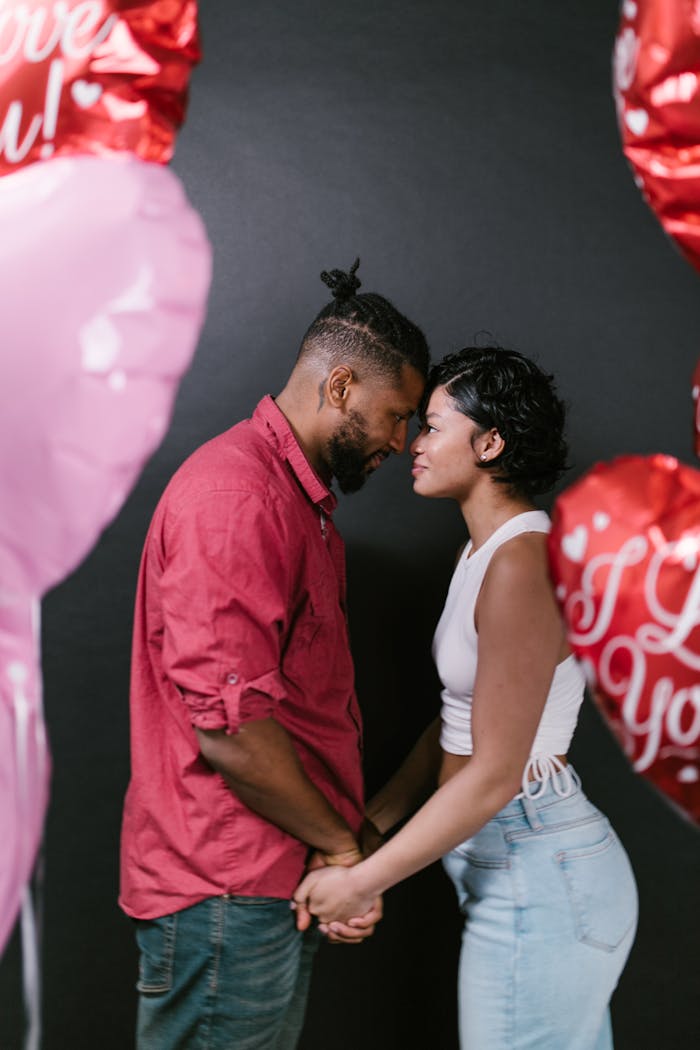 Affectionate couple in love holding hands surrounded by heart-shaped balloons.