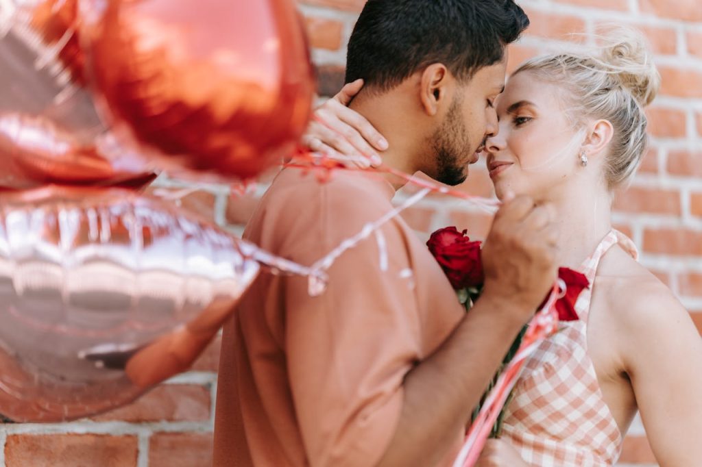 A romantic moment between an interracial couple with heart-shaped balloons and red roses.
